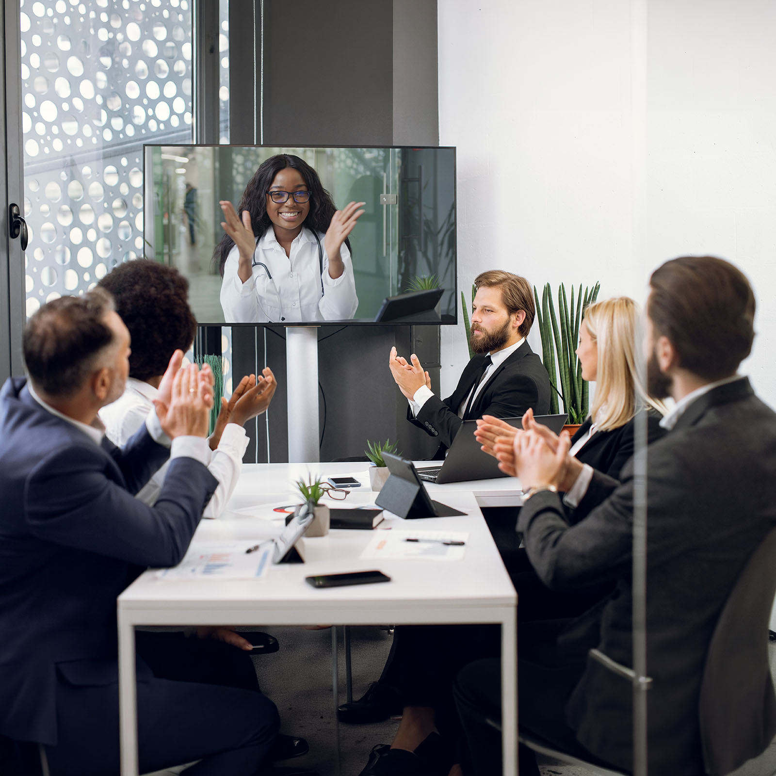 Equipe corporativa em reunião de governança, acompanhando indicadores por videochamada com tablets e notebook sobre a mesa
